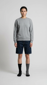 Model i grå sweatshirt, mørkeblå denimshorts og umage sokker på en hvid baggrund.