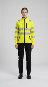 Kvinde i gul high-visibility jakke med refleksstriber og sorte bukser mod en grå baggrund.