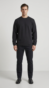 Mand stående i en sort sweatshirt og sorte bukser mod en lys grå baggrund.