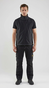 Mand iført sort softshell-vest og arbejdsbukser med hvide syninger mod en lys baggrund.