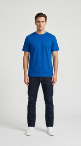 Mand i en klar blå t-shirt, mørke jeans og hvide sneakers på en lys baggrund.