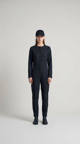 Kvinde iført en sort langærmet jumpsuit og kasket mod en lys grå baggrund.