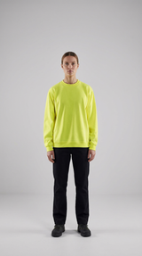 Kvinde i neon gul sweatshirt og sorte bukser mod en neutral grå baggrund.