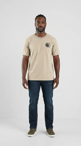 Mand i beige Carhartt-t-shirt, mørkeblå jeans og grønne sneakers mod en hvid baggrund.