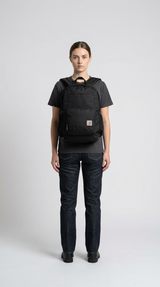 En kvinde iført en sort Carhartt-rygsæk, mørk t-shirt og jeans mod en hvid baggrund.