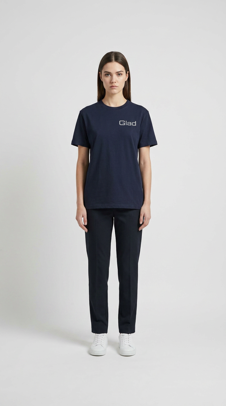 Kvinde i mørkeblå t-shirt med Glad-logo, mørke bukser og hvide sneakers mod en hvid baggrund.