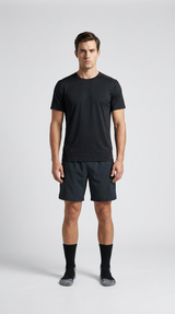 Mand i sort t-shirt, mørke shorts og sorte strømper mod en lys grå baggrund.