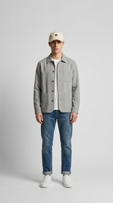 Mand i grå overshirt, hvid t-shirt, blå jeans og beige kasket mod en lys baggrund.