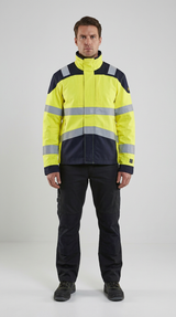 Mand i gul og mørkeblå high-vis arbejdsjakke med refleksstriber og mørke arbejdsbukser foran en lys baggrund.