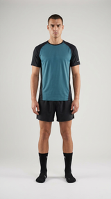 Mand i blågrøn og sort sports-t-shirt, sorte shorts og sorte strømper mod en lys baggrund.
