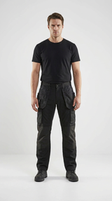 Mand i sort t-shirt og sorte arbejdsbukser med praktiske lommer foran en hvid baggrund.