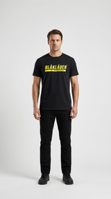 Mand i sort Blåkläder t-shirt og sorte bukser stående mod en hvid baggrund.