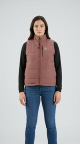 Kvinde i en støvet rosa quiltet vest, sort trøje og blå jeans mod en lys baggrund.