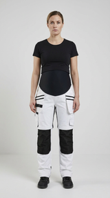 Gravid kvinde i hvide og sorte arbejdsbukser med mavepanel og sort t-shirt foran en lys baggrund.