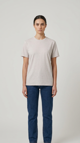 Kvinde iført en lysegrå t-shirt og mørkeblå jeans mod en lys, neutral baggrund.