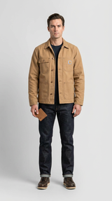 Mand i sandfarvet Carhartt-jakke og mørke jeans holder en læderpung mod en grå baggrund.