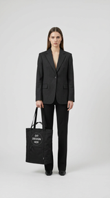 Kvinde i mørk blazer holder en sort mulepose med teksten 'DIT DESIGN HER' mod en lys baggrund.