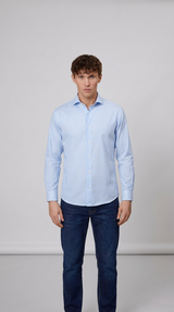 Mand iført lyseblåstribet skjorte og mørkeblå jeans mod en neutral baggrund.