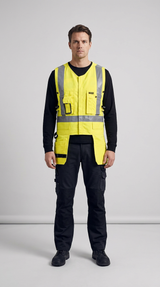 Mand i gul refleksvest med værktøjslommer og sorte arbejdsbukser på en grå baggrund.