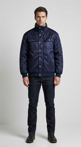 Mand i mørkeblå jakke med høj krave, mørke jeans og støvler mod en lys baggrund.