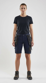 Kvinde i sort t-shirt, mørkeblå arbejdsshorts med lommer og arbejdsstøvler på hvid baggrund.