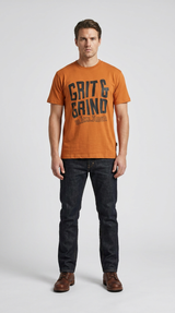 Mand i orange t-shirt med 'Grit & Grind' tekst, mørke jeans og brune læderstøvler på hvid baggrund.