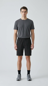 Mand i grå t-shirt, sorte shorts og grå sneakers på en lys baggrund.