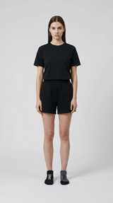 Kvinde i sort t-shirt og shorts med en sort og en grå sok foran en lys grå baggrund.