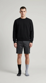 Mand i sort sweatshirt, grå shorts og umage sokker mod en lys baggrund.