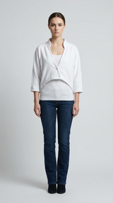 Kvinde iført hvid kort cardigan, hvid top og mørkeblå jeans på en grå baggrund.