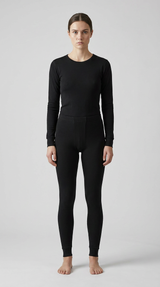 Kvinde i sort langærmet termoundertøj og matchende leggings mod en grå baggrund.