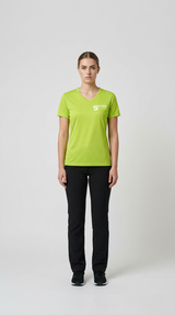 Kvinde iført limegrøn v-hals t-shirt med logo og sorte bukser på en lys baggrund.