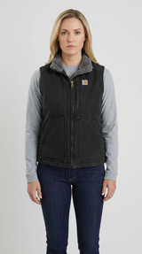 Kvinde i sort Carhartt-vest med fleece-krave, grå langærmet trøje og blå jeans på en lys baggrund.