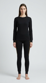 Kvinde i sort langærmet trøje og sorte leggings med gul sidestribe mod en grå baggrund.