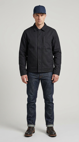 Mand iført en sort jakke, mørkeblå jeans og en blå kasket mod en neutral baggrund.