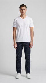 Mand i hvid v-hals t-shirt, mørkeblå jeans og hvide sneakers mod en grå baggrund.
