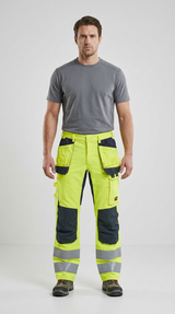 Mand i grå t-shirt og neon-gule arbejdsbukser med refleksstriber mod en hvid baggrund.