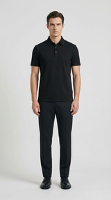 Mand i sort polo-shirt, sorte bukser og sorte sko stående mod en lys grå baggrund.