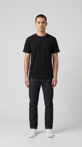 Mand i sort t-shirt og mørkeblå jeans stående mod en grå baggrund.