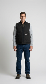 Mand i sort Carhartt-vest, grå trøje, blå jeans og støvler mod en hvid baggrund.