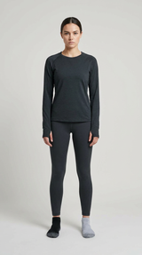 Kvinde i mørkegrå langærmet trøje, sorte leggings og umage sokker foran en lys grå baggrund.