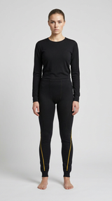 Kvinde i sort langærmet undertrøje og leggings med gule syninger på benene mod en grå baggrund.