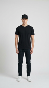 Mand i sort t-shirt, sort kasket, mørke jeans og hvide sneakers mod en lys baggrund.