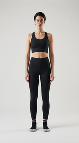 Kvinde i sort sports-bh og leggings stående mod en lys grå baggrund.