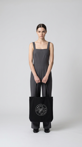 En kvinde i gråt jumpsuit holder en sort mulepose med Classic Coffee-logoet.