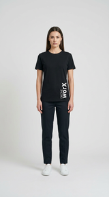 Kvinde i sort Drone Worx t-shirt, sorte bukser og hvide sneakers mod en lys baggrund.