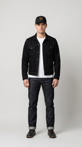 Mand i sort denimjakke, hvid t-shirt, mørke jeans og kasket mod en lysegrå baggrund.