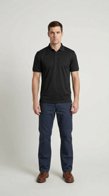 Mand i sort polo shirt og mørkeblå bukser stående foran en lys baggrund.