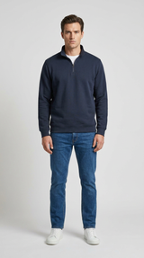 Mand i mørkeblå sweatshirt med lynlås, blå jeans og hvide sneakers på en lys baggrund.