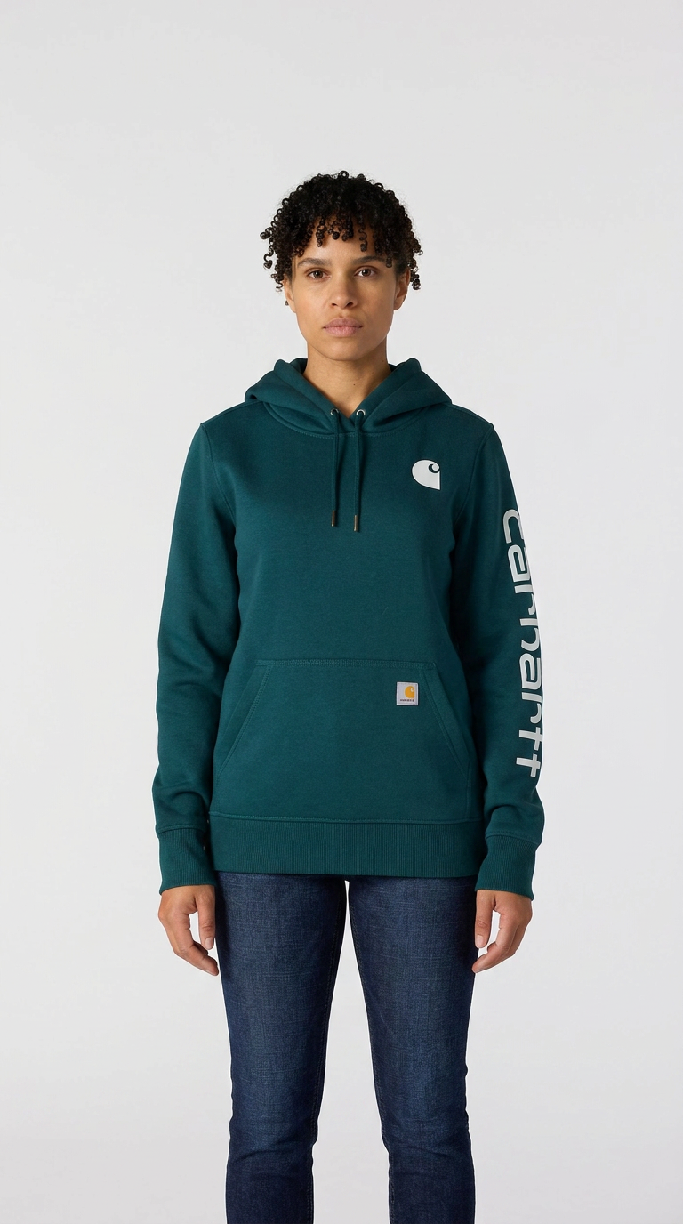 Kvinde i mørkegrøn Carhartt-hættetrøje og blå jeans foran en hvid baggrund.